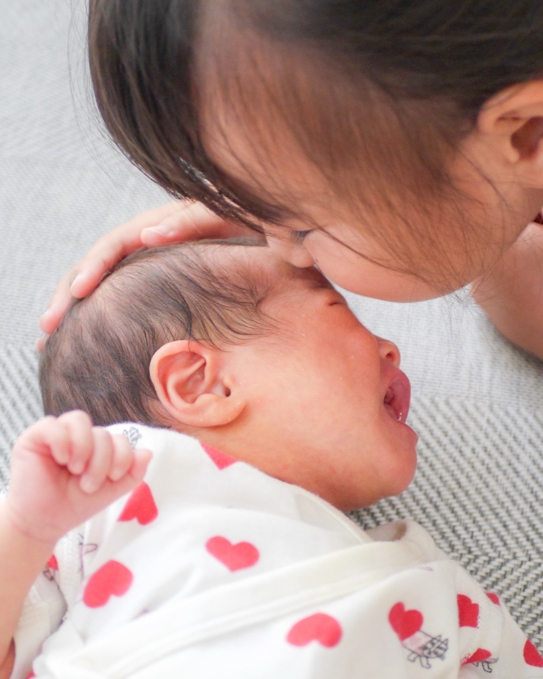 茅ヶ崎のご自宅で、5歳のお姉ちゃんが新生児の妹に優しくキスをしているニューボーンフォト。姉妹の温かな絆を感じる一瞬。