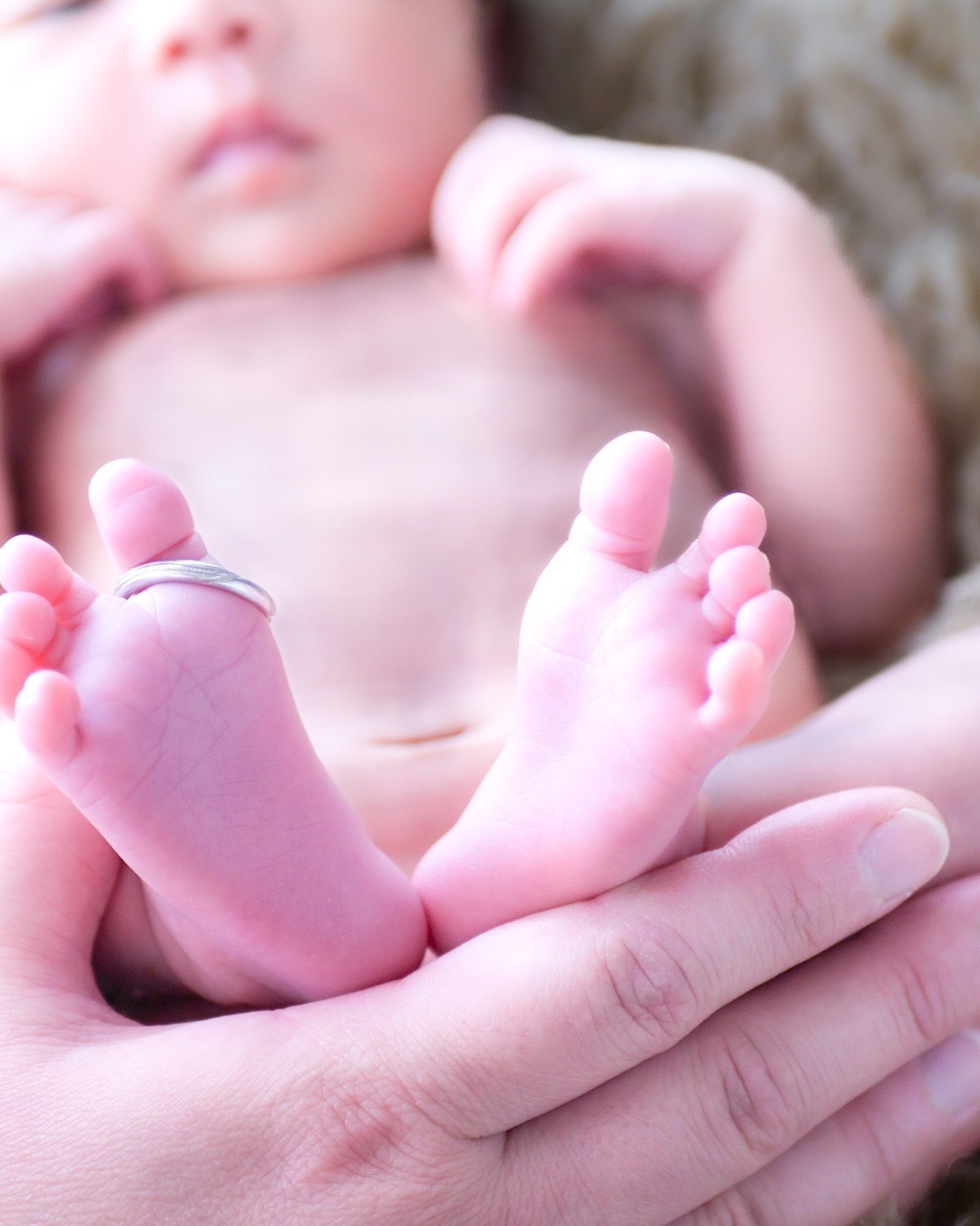 港区のご自宅で撮影されたニューボーンフォト。赤ちゃんの小さな足にママの結婚指輪をそっと乗せた愛らしい一枚。家族の絆と赤ちゃんの可愛らしさが感じられる特別な瞬間。