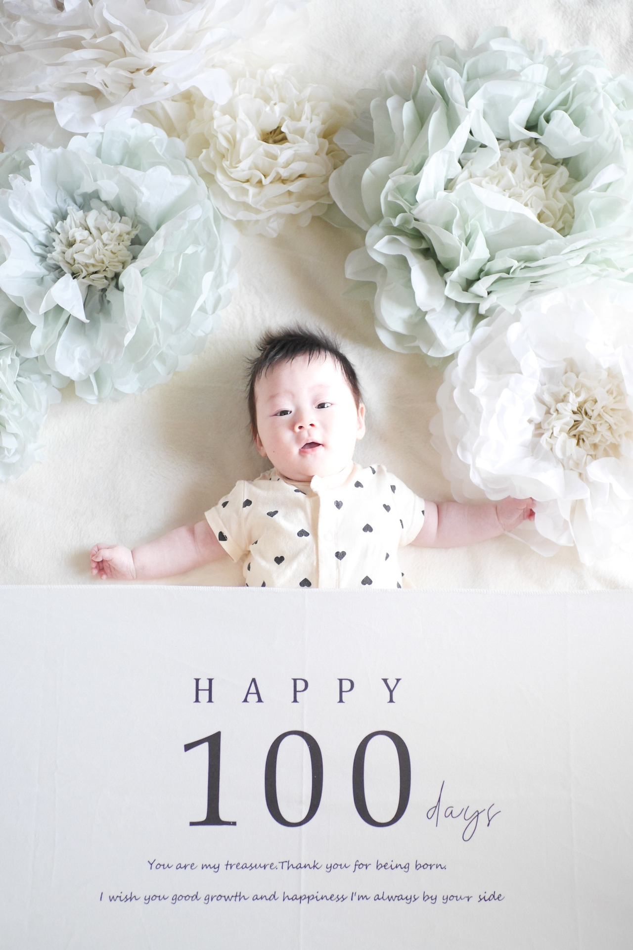 生後100日を迎えた赤ちゃんが白い背景で穏やかに過ごしている姿。