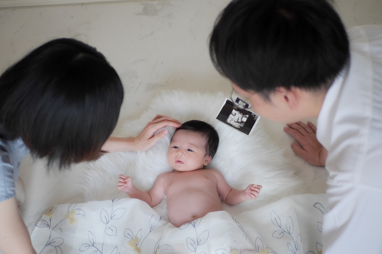 自宅でリラックスする赤ちゃんと両親の自然な笑顔を残すニューボーンフォト・お宮参り撮影