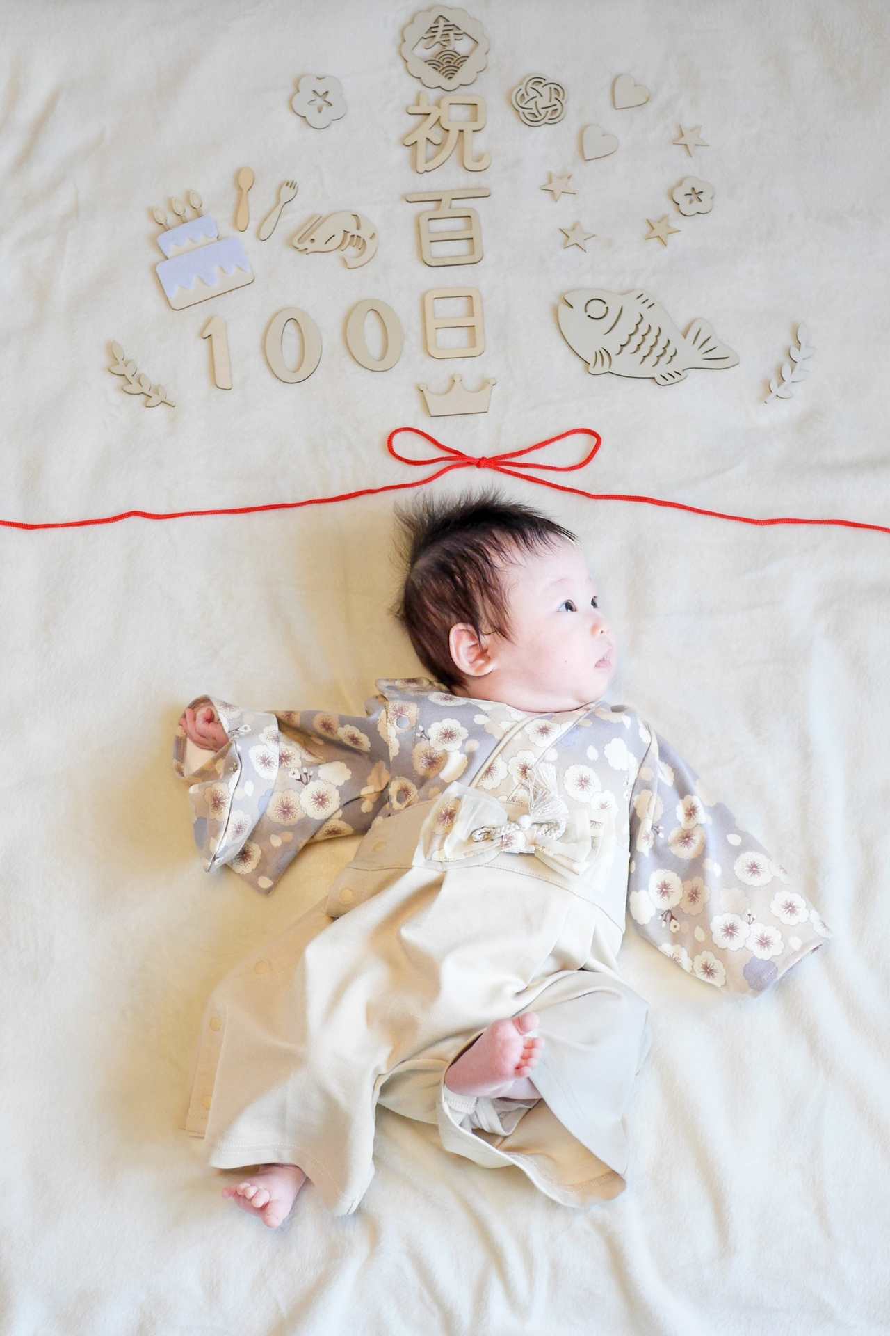 鯛やエビのミニチュア飾りに囲まれた赤ちゃん、生後100日を祝う自宅撮影の記念フォト。」